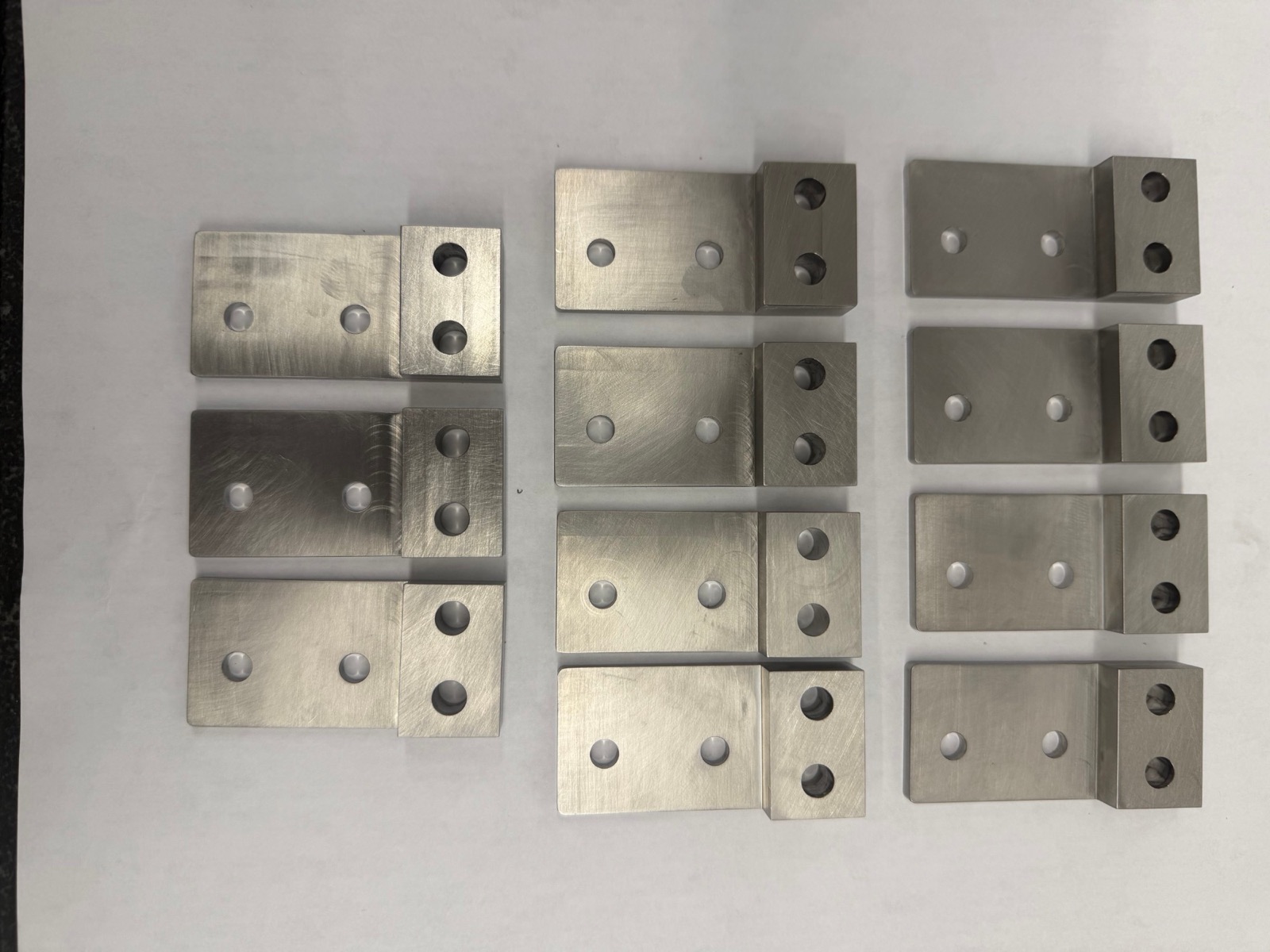 Twelve identical milled brackets laid out in three columns