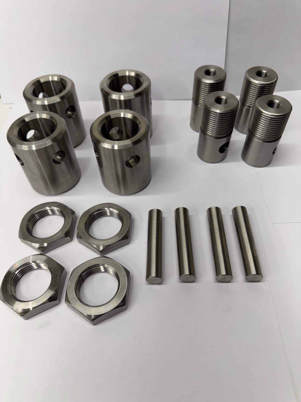 A set of machined stainless parts: cross-drilled bushings, threaded adapters, hex nuts and pins