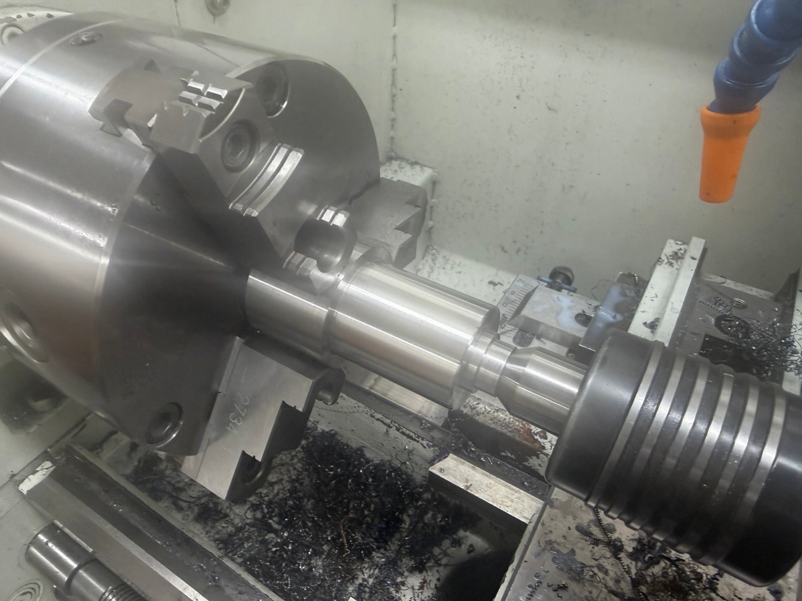 A steel part being turned on a lathe, held in a three-jaw chuck and supported by a live center