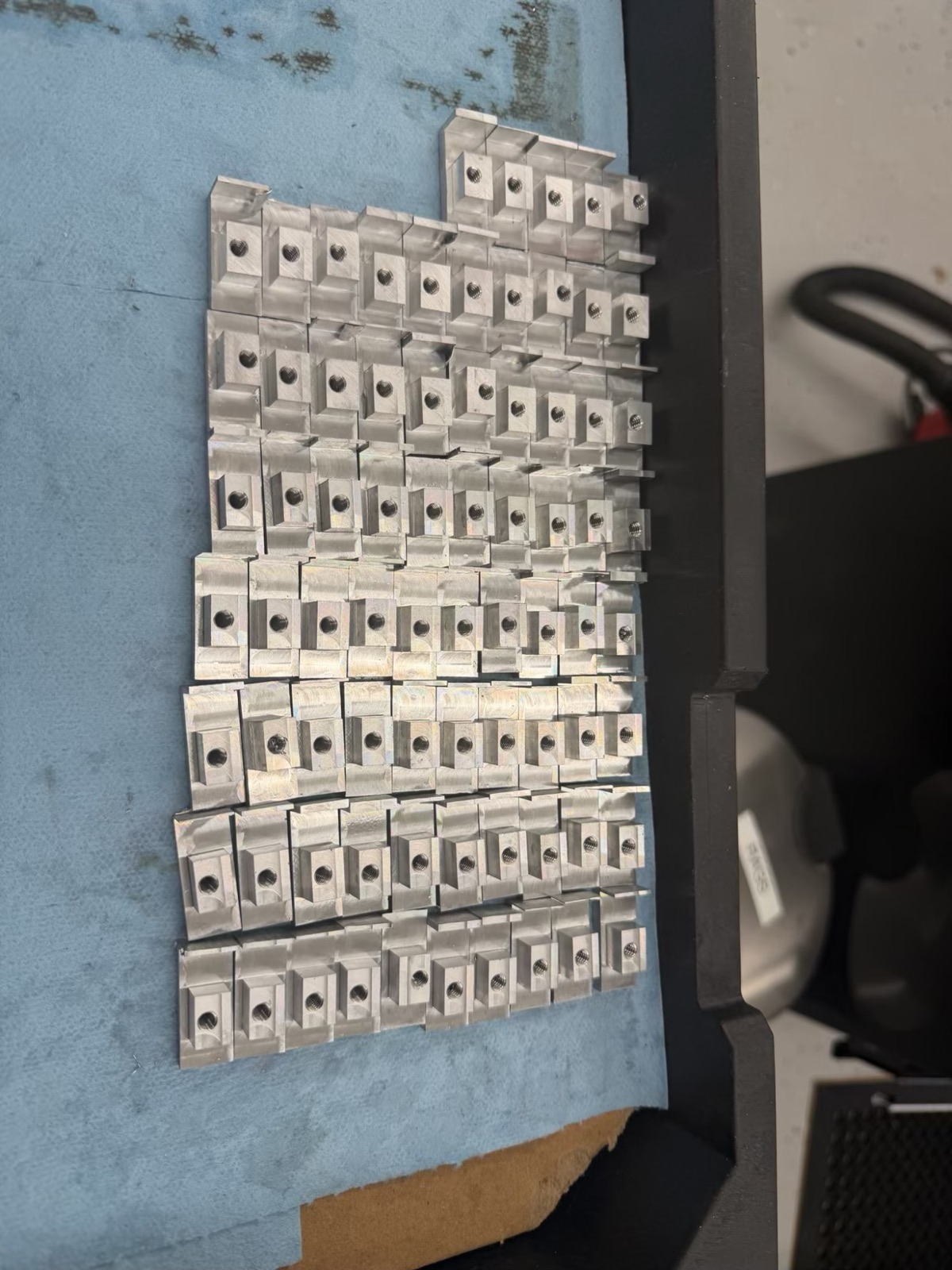 A batch of dozens of identical milled T-nuts with tapped holes, laid out in rows